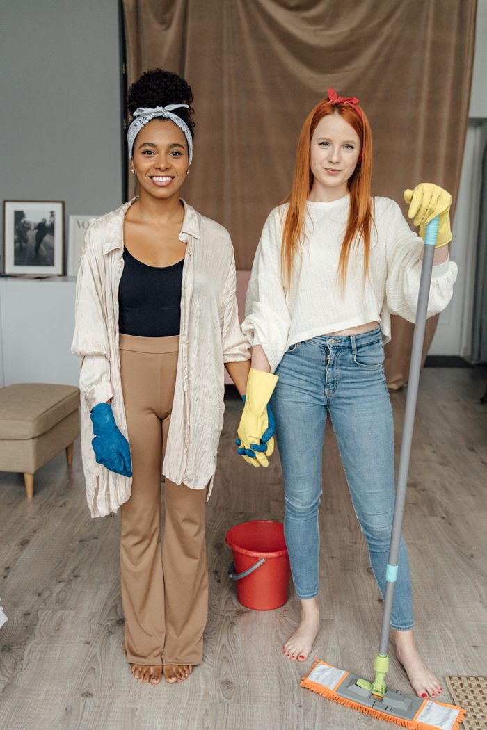 services-01 Two women smiling and holding hands while cleaning indoors, symbolizing teamwork.